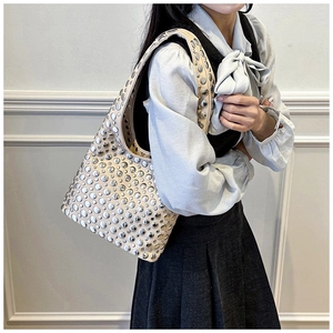 Detail of beige hobo bag with silver metallic rivets worn as a stylish underarm shoulder bag