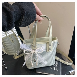 Detail of light green woven handbag with pearl bow charm and adjustable shoulder strap