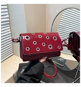 Macro view of burgundy patent leather shoulder bag with silver eyelets and side profile