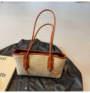 Detail of hand-woven straw tote bag with brown leather handles on a dark background