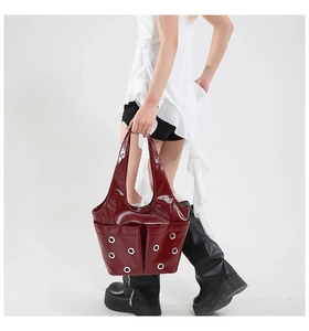 Detail of burgundy glossy tote bag with large silver grommets shown on model