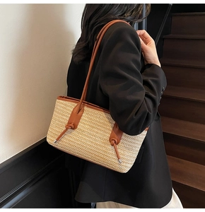 Detail view of woven straw tote bag with brown leather knotted strap on a model