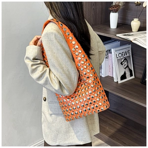 Model wearing bright orange leather underarm bag with silver rivets and wide strap