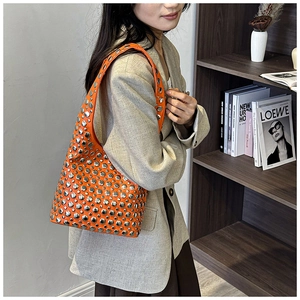 Detail view of bright orange studded underarm bag with silver rivets and glossy leather