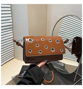 Detail of a brown glossy leather crossbody bag with silver eyelets and multi-layer design