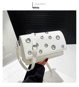 Close-up of white baguette bag with silver grommets and adjustable shoulder strap