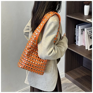 Detail of bright orange underarm bag featuring silver rivets and glossy leather texture