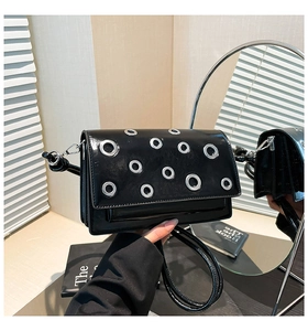 Detail of black patent leather crossbody bag with silver eyelets and sleek shoulder strap