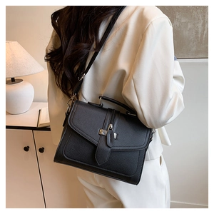 Detailed view of black litchi grain shoulder bag worn with white blazer