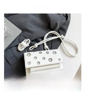 Detailed view of a white crossbody bag with silver eyelets displayed on a gray blazer