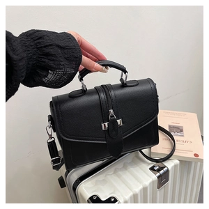 Close-up of black lychee grain leather handbag with silver hardware on white suitcase