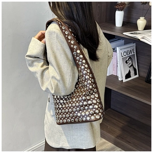 Close-up of a brown leather underarm bag with silver rivet details on a model