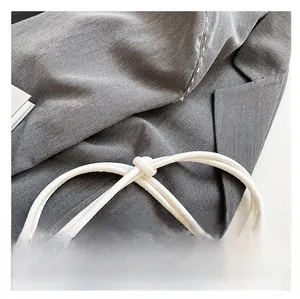 Detail of grey twill fabric and white leather knotted shoulder strap on a baguette bag