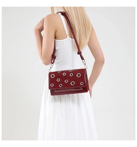 Detail of burgundy crossbody bag with silver eyelets on a model in white dress