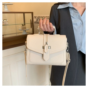 Close-up of model holding a beige litchi-grain leather handbag in a cozy cafe setting