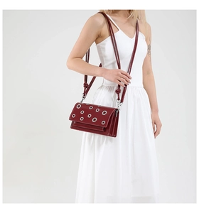 Detail view of burgundy crossbody bag with silver eyelets on glossy leather finish