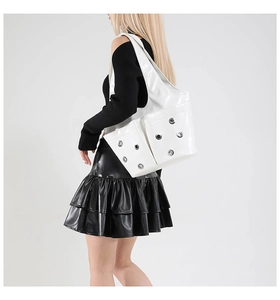 Detail of white glossy tote bag with metal eyelet pockets on shoulder of model