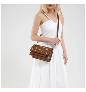 Detail of coffee brown glossy leather crossbody bag with silver metal eyelet hardware