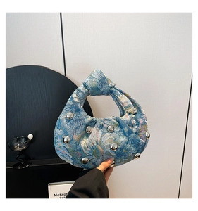 Detailed blue floral brocade handbag with silver studs and knotted handle held by a model