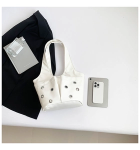 Detail of off-white PU shoulder bag featuring twin front pockets and silver metal eyelets
