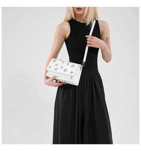 Detailed view of a white square crossbody bag with silver eyelet rivets on a black dress