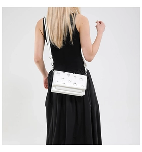 Close-up of white crossbody bag with silver eyelet studs and knotted leather shoulder strap