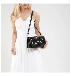 Detail of black leather crossbody bag featuring silver eyelet studs and flap closure