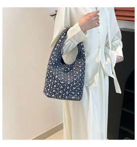 Detail of denim bucket bag with silver studs held by a model in a white dress