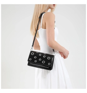 Close-up of black glossy crossbody bag with silver eyelet studs on a white studio background