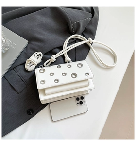 Detailed view of white rectangular crossbody bag with silver eyelets and dual straps