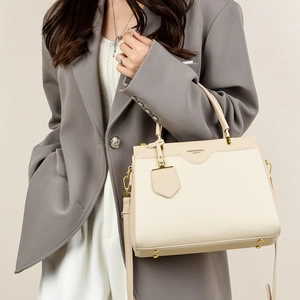Detail of a cream textured shoulder bag with leather trim and gold metal hardware