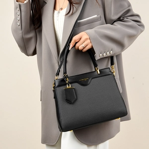 Detail of cross-grain black leather handbag with gold hardware and logo on grey suit