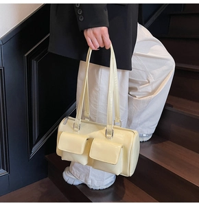 Close-up of beige cylindrical pillow bag featuring dual front pockets on wooden steps