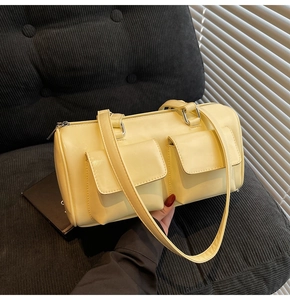 Close-up of beige cylindrical pillow bag featuring double front pockets and silver hardware