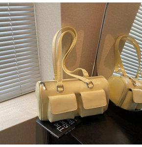 Detail of cream yellow glossy barrel bag with dual front pockets and side lighting