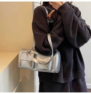 Detailed view of silver metallic cylindrical bag with dual flap pockets and thin strap