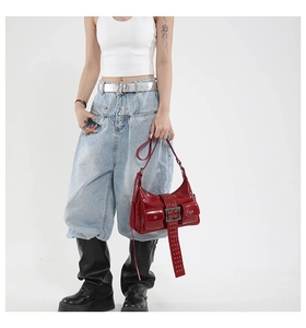 Detail of red glossy leather shoulder bag featuring Y2K rivets and functional pockets