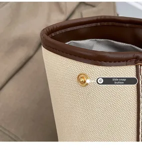Détail du bouton-pression latéral sur le cabas en toile beige et cuir brun