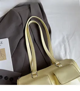 Detail of a pale yellow leather shoulder bag with two front pockets on a grey suit jacket