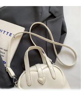 Detail of cream PU shell bag showing heart buckle and adjustable shoulder strap