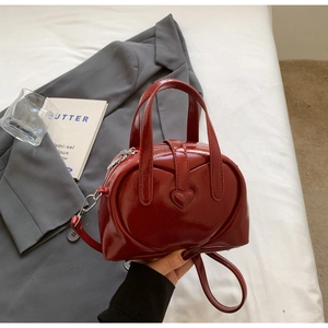 Macro detail of glossy wine red heart-shaped leather handbag on white fabric