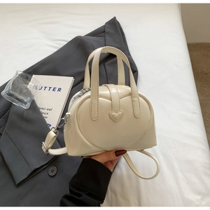 Close-up of cream PU leather shell bag with embossed heart detail on a white bed
