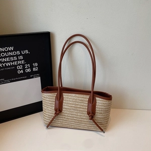 Bohemian woven straw tote bag with brown leather handles and decorative knots on white background