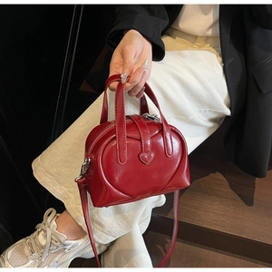Detail of red heart-shaped PU leather handbag with glossy finish and matching top handles