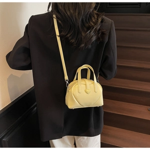 Close-up of bright yellow PU shell bag with a heart accent on a black blazer outfit