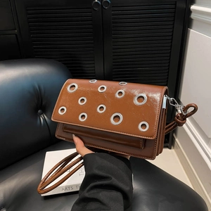 Brown stud crossbody bag with silver eyelets and cylindrical strap in fashion setting