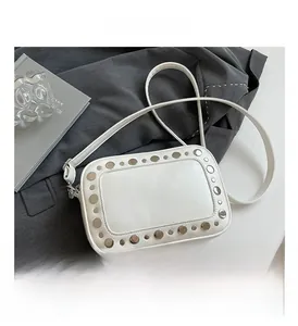 Detailopname van witte crossbodytas met zilveren studs op een grijze blazer