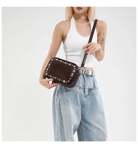 Detail van donkerbruine leren crossbodytas met zilveren studs gedragen door model