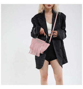 Borsa a mano rosa con borchie e nappe indossata su un abito nero testurizzato