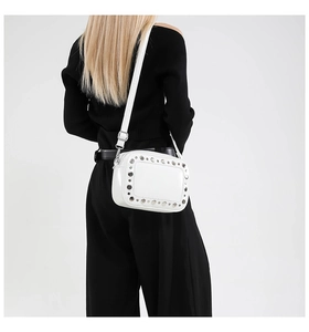 Crossbody weergave van een witte leren tas met zilveren klinknagels en verstelbare riem